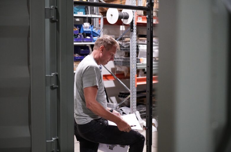 Designer Esa Nurmi reviews drawings and makes notes in a storage space surrounded by shelves and tools.