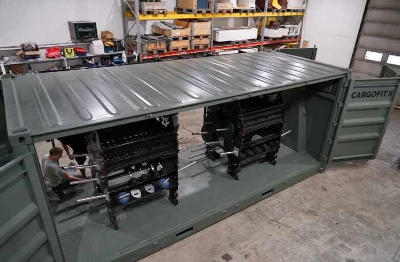 Inside the container structure, versatile gym equipment is installed while a worker checks the details.