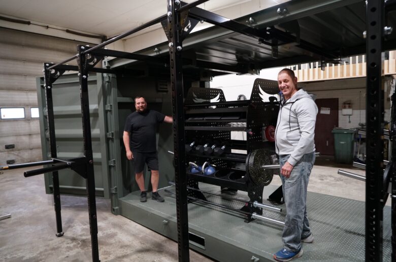 Perttu Huuhka and Petri Huuhka smile in front of the completed container gym setup in the workshop.