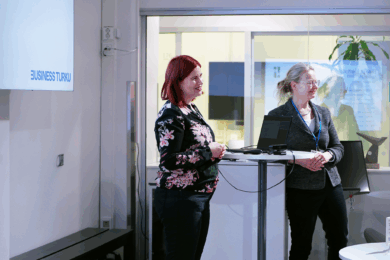 Kaksi naista pitää puhetta valkoisen pöydän ääressä