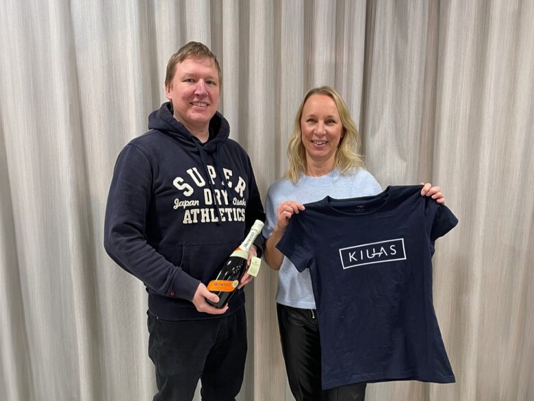 Mikko Hällfors ja Hanna Kalliobiemi poseeraavat yhdessä; Hällfors pitää kädessään lahjapulloa ja Kallioniemi pitelee t-paitaa, jossa lukee ‘KIUAS’.”