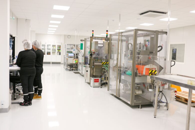 Puhdastilassa toimiva tuotantotila, jossa työntekijät valvovat lääkinnällisten tuotteiden pakkauslinjaa suojavaatetuksessa.