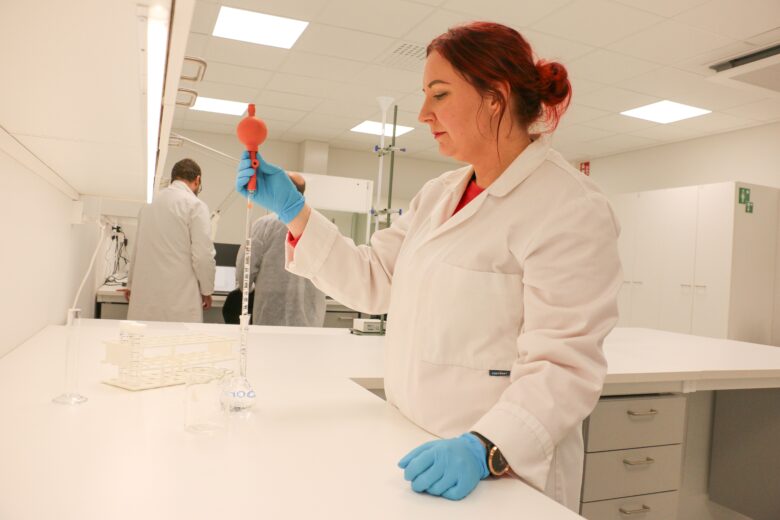 Laboratoriotyöntekijä pipetoi nestettä mittalasiin modernissa laboratoriossa suojakäsineet kädessään.