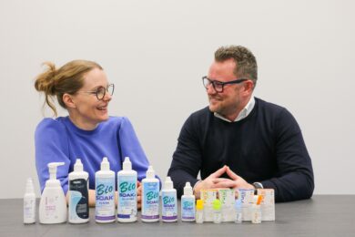 Kaksi henkilöä istuu pöydän ääressä ja esittelee silmänhoitotuotteita, jotka on aseteltu riviin pöydälle.