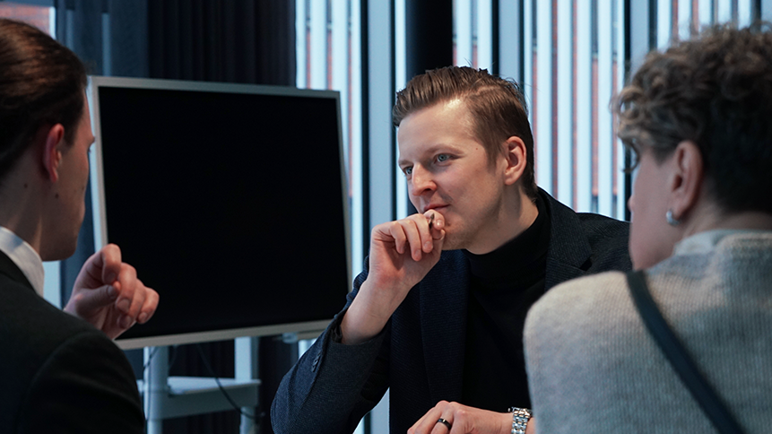 Asiantuntija keskustelee kahden asiakkaan kanssa, jotka ovat selkäpäin kameraan.