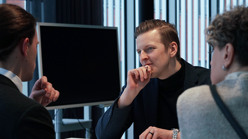 Asiantuntija keskustelee kahden asiakkaan kanssa, jotka ovat selkäpäin kameraan.