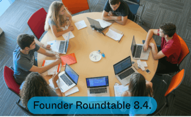 A group of people sitting around a round table, working on laptops, notebooks, and papers. The table is light‑coloured and surrounded by brightly coloured chairs. A blue banner at the bottom of the image displays the text Founder Roundtable 8.4.