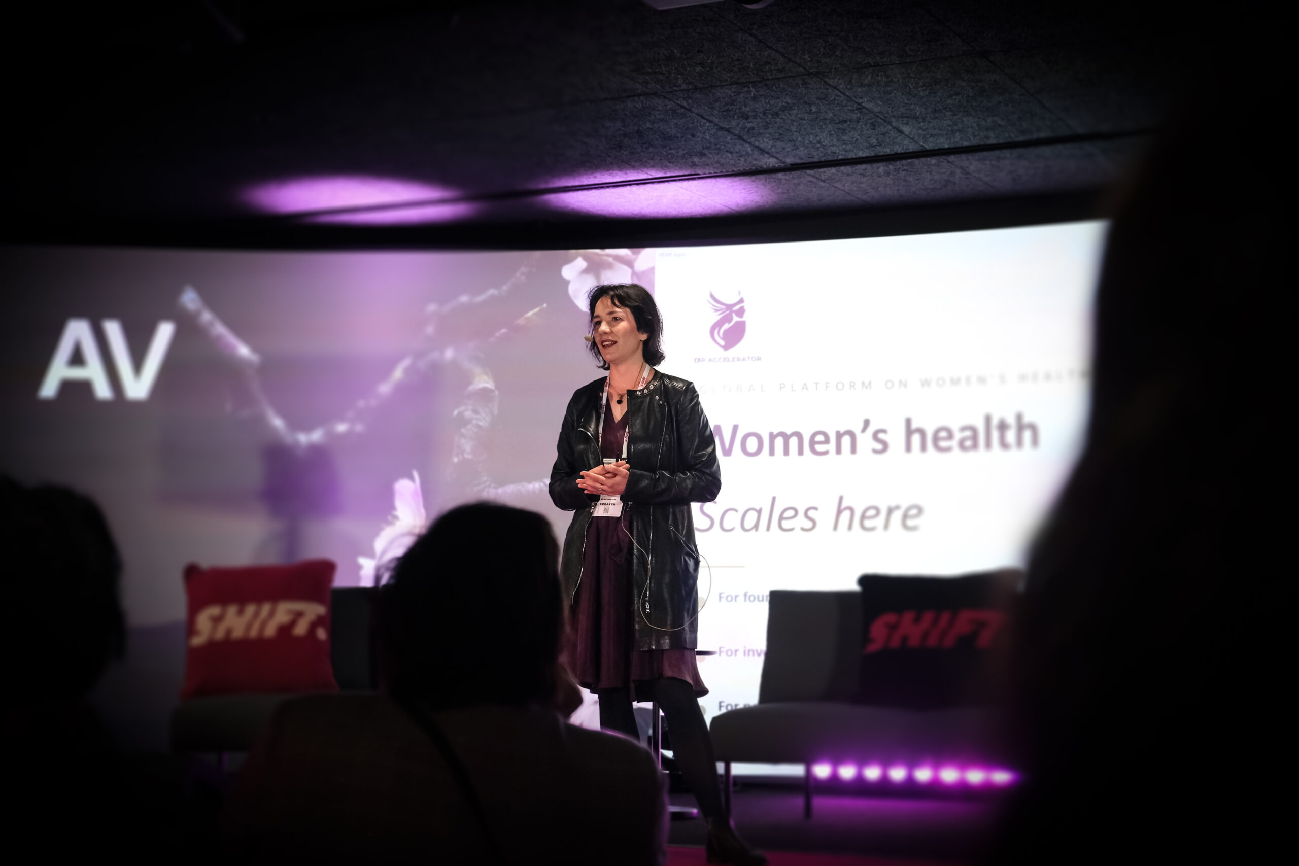 Anastasiya Markvarde puhuu lavalla SHIFT-tapahtumassa, taustalla “Women’s health scales here” -dia.