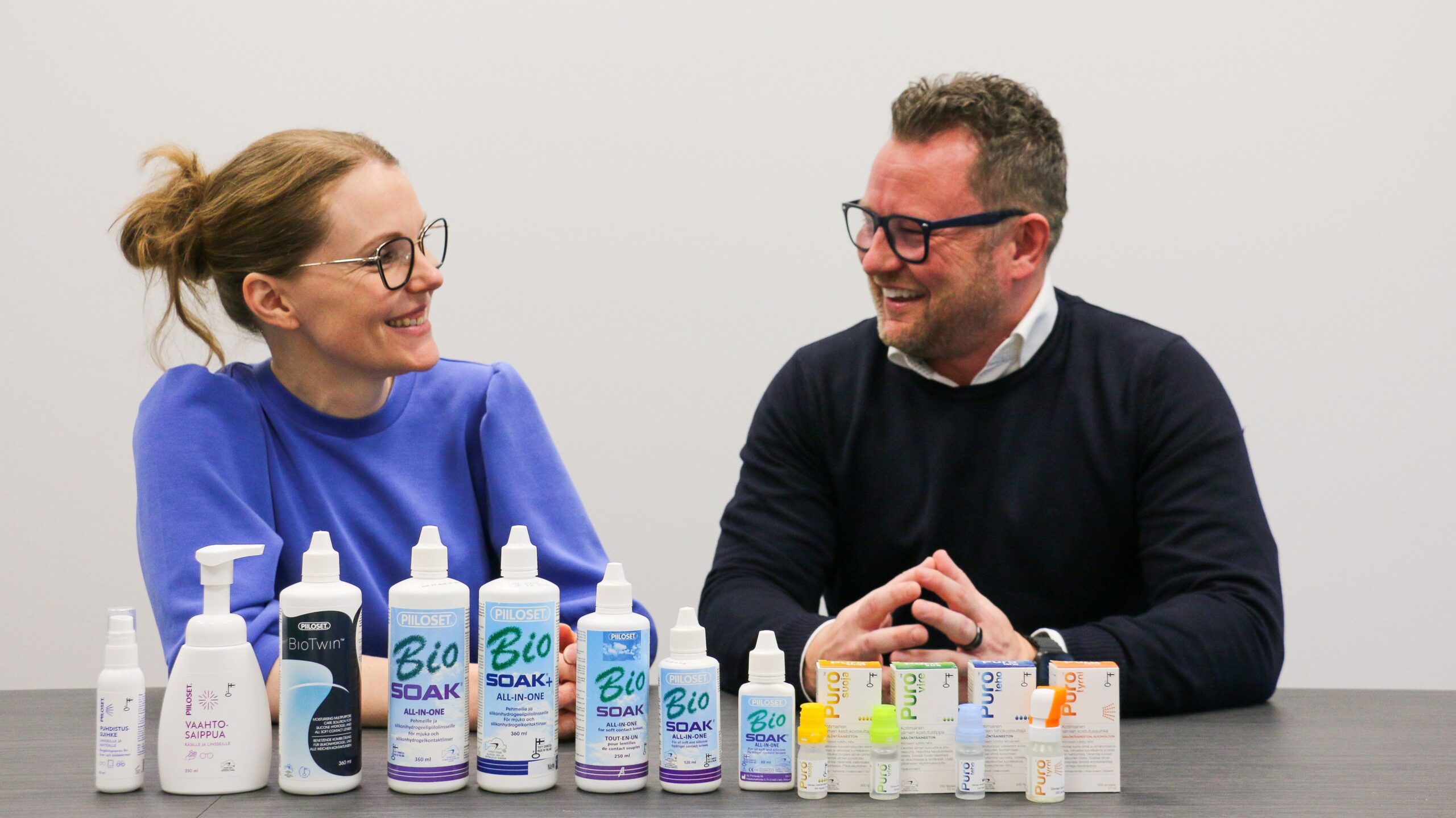 Two people seated at a table presenting a range of eye care products arranged in a row.