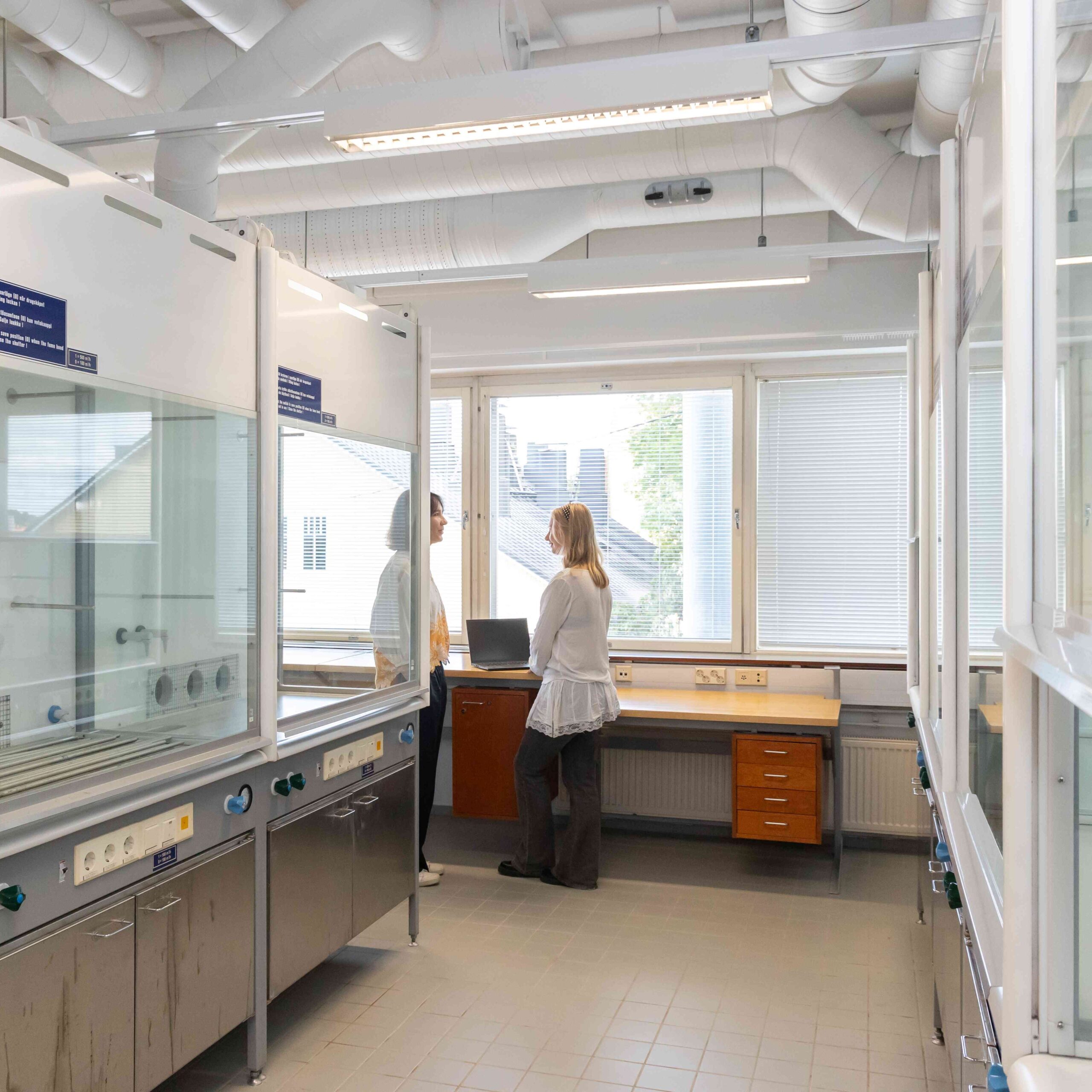 Kaksi naista laboratoriotilan perällä työpöydän ääressä keskustelemassa.