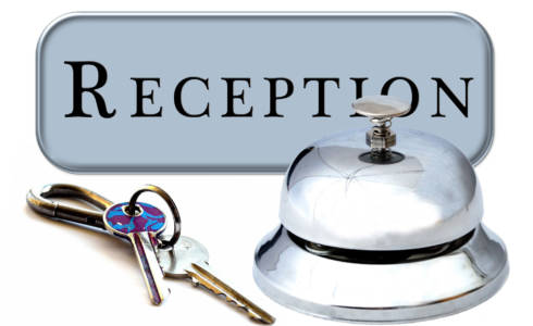 Reception -kyltti, soittokello ja hotellihuoneen avaimet valkoisella tautalla asetelmana.