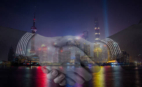 Aasialainen suurkaupunki yövalaistuksessa. Kuvan päällä kättelevät kädet.
