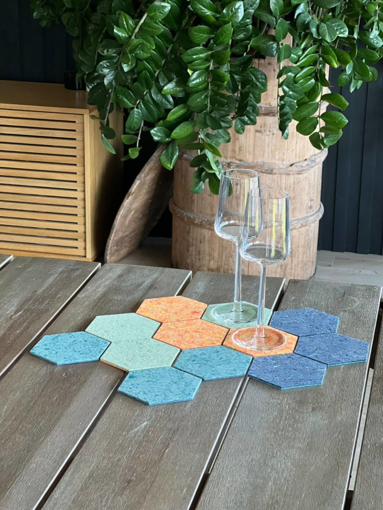 Rester fibre is used to make blue, orange and green polygonal coasters, among others. Two empty wine glasses sit on top of the coasters. 